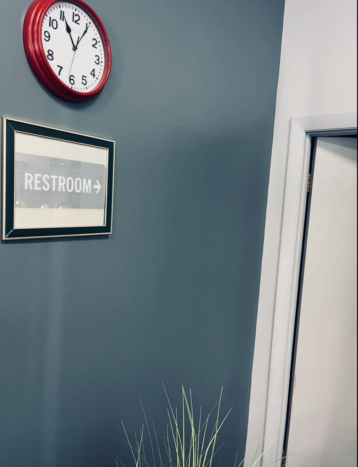 Red wall clock above the framed restroom sign